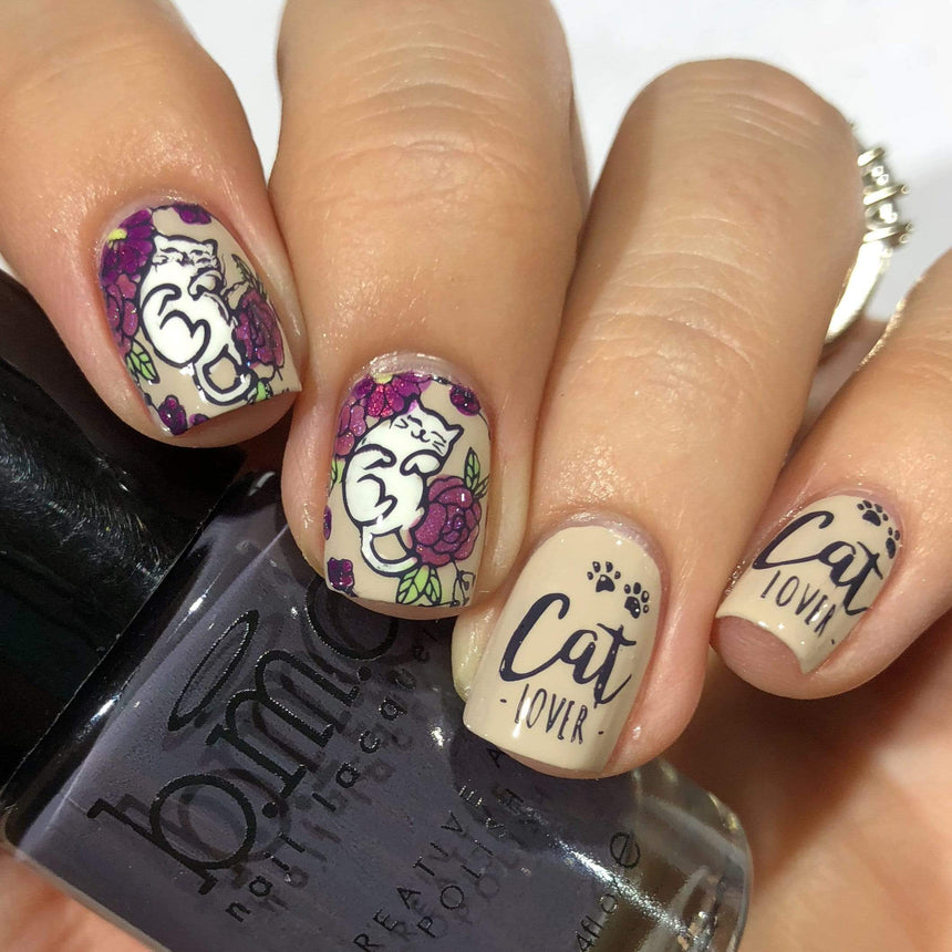A manicured hand with flowers and cats design holding a polish.