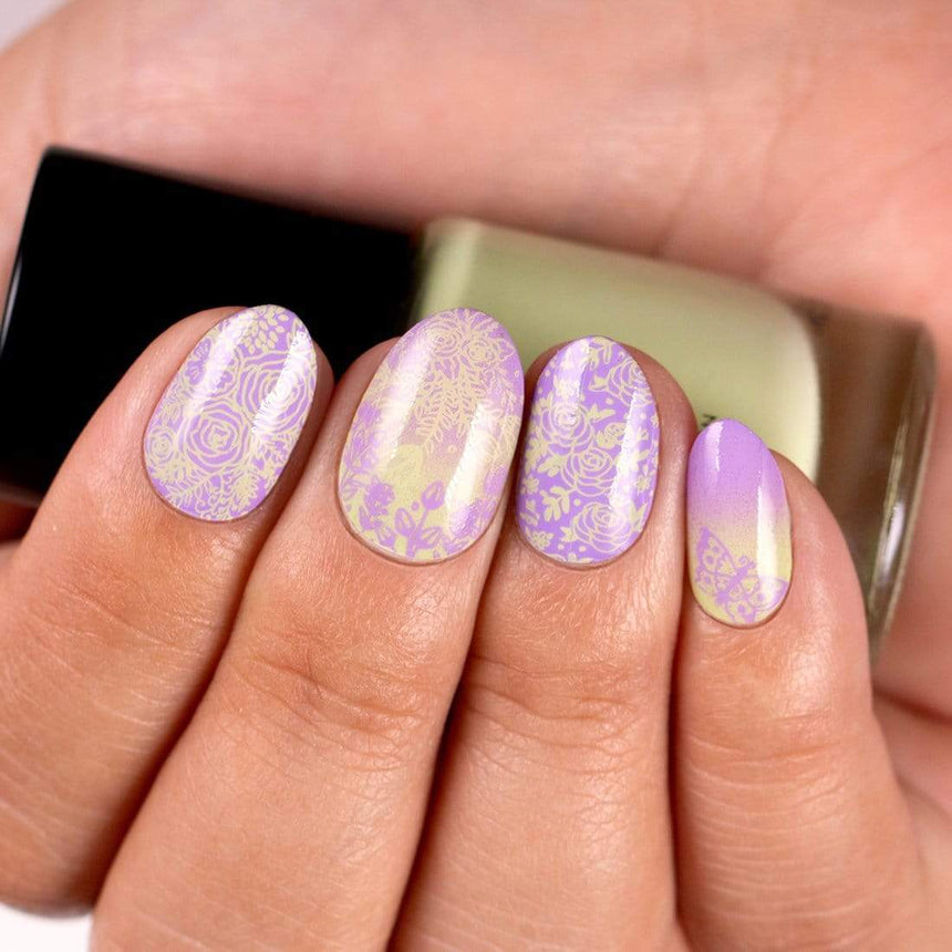 A manicured hand in purple with a garden variety design and a butterfly holding a polish.
