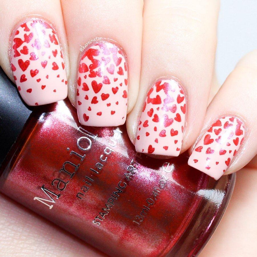 A manicured hand in full of hearts design holding a polish by Maniology.