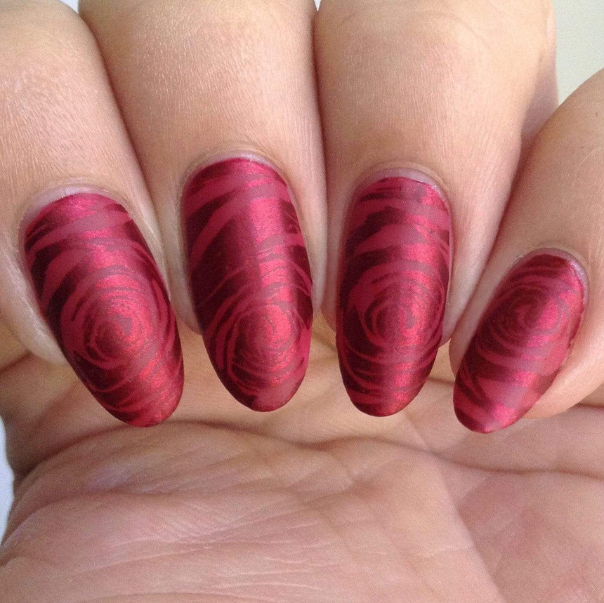 A manicured hand in red with floral design by Maniology (m179).