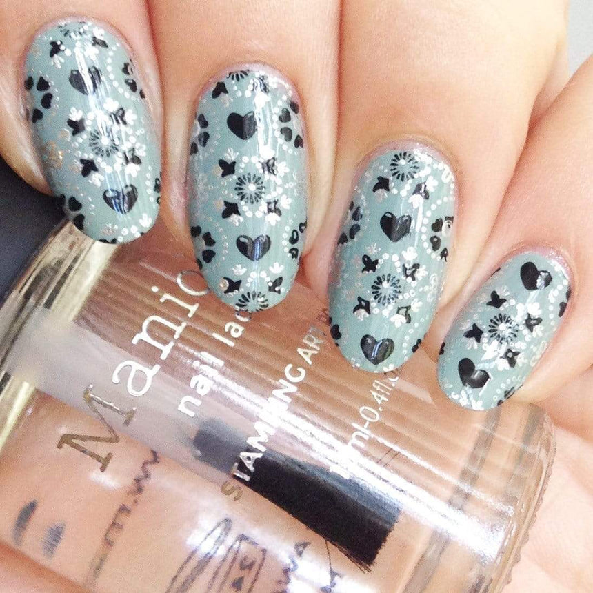 A manicured hand made with Shangri La (B296) Dusty Blue Stamping Polish holding a top coat by Maniology.