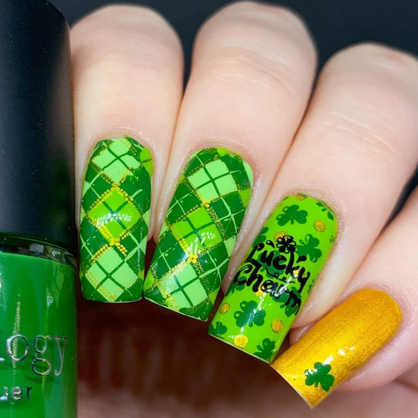 A manicured hand with clovers design holding a stamping polish by Maniology (m188).