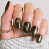 Hand with black and gold Maniology magnetic nail polish on a neutral background