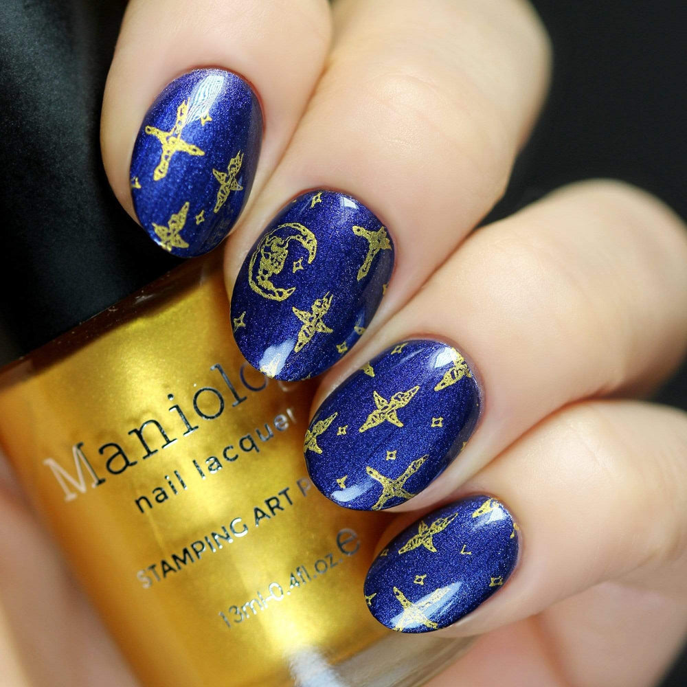 A manicured hand in blue with moon and stars designs holding a polish by Maniology (m159).