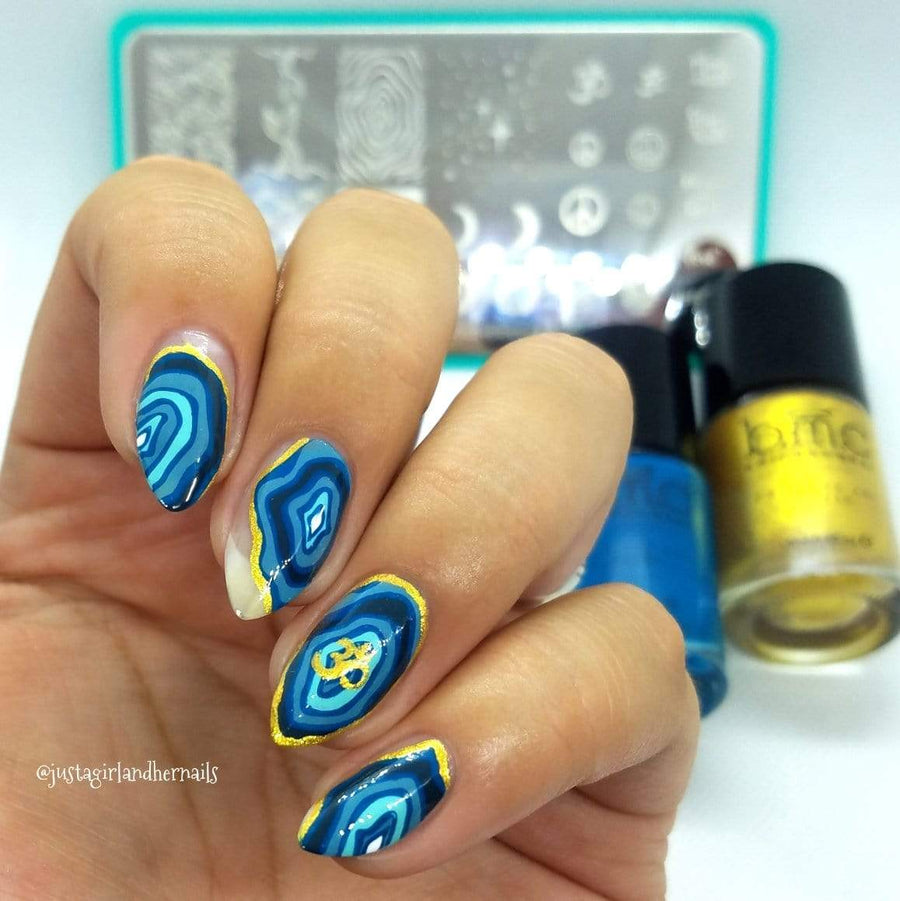  A manicured hand in blue and yellow with justagirlandhernails design by Maniology in front of a stamping plate and 2 polishes.