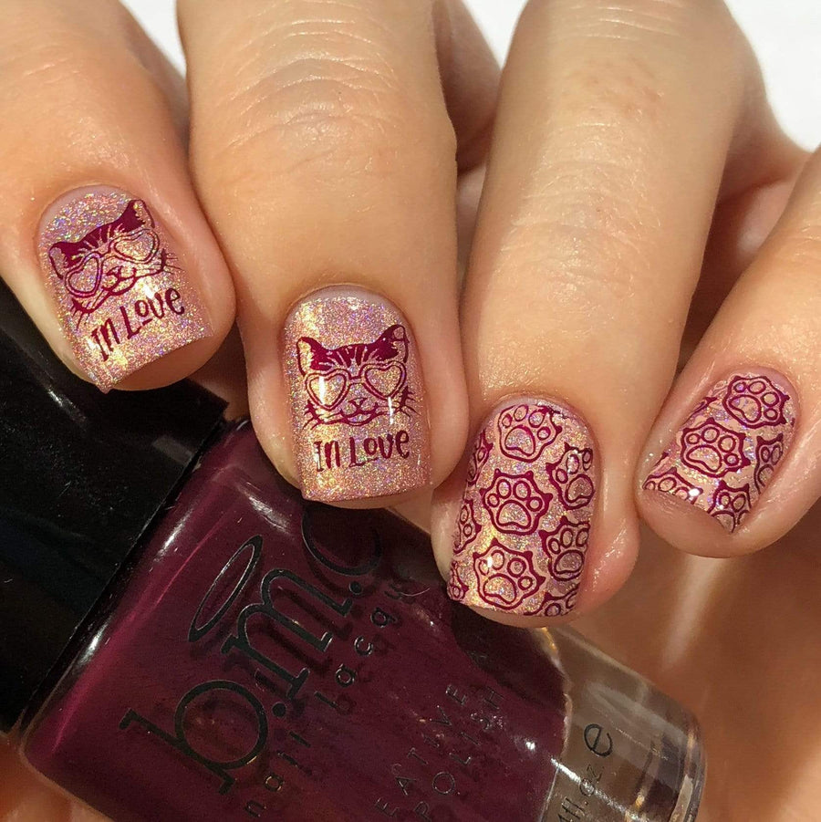 A manicured hand in glitters with cats and paws design holding a polish.