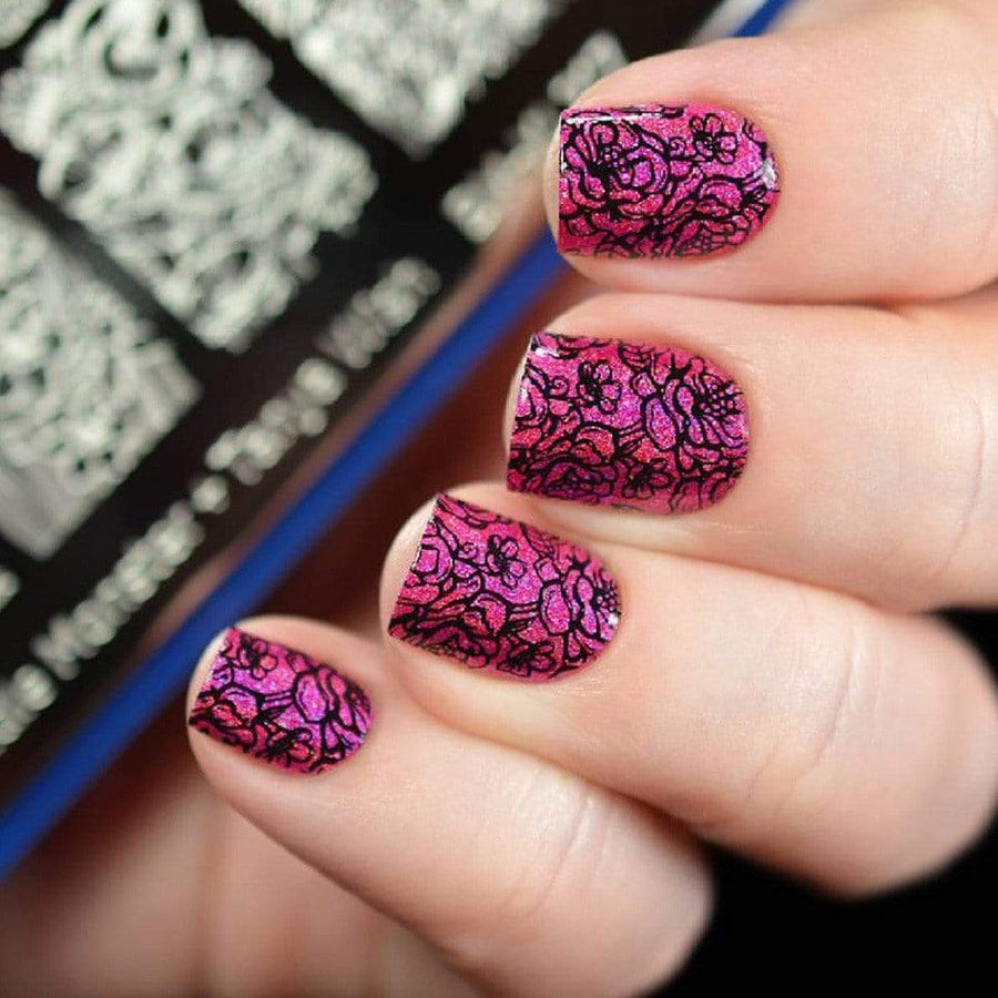 A manicured hand in pink with floral designs holding a stamping plate.