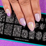  A manicured hand in purple with a garden variety design over a stamping plate.