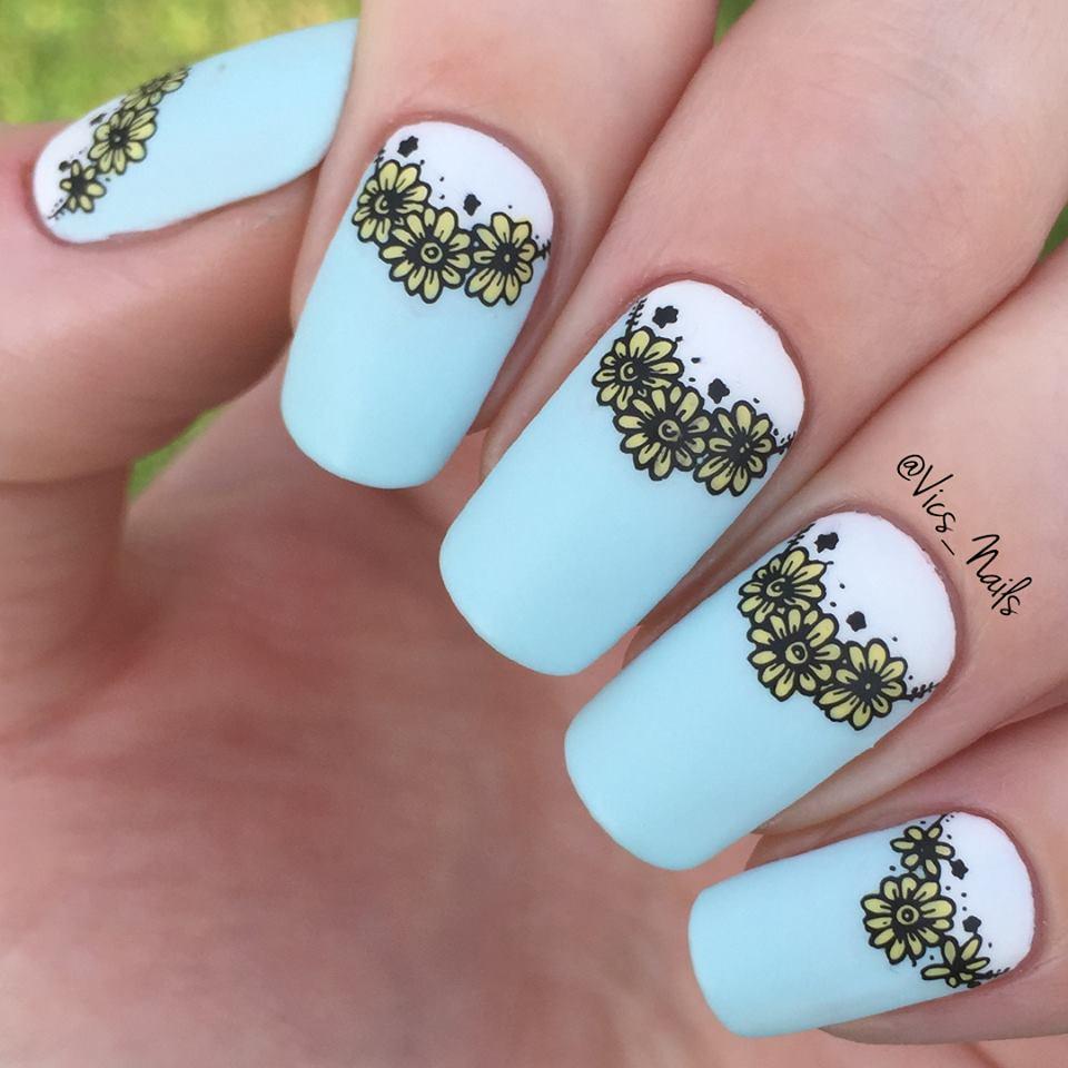 A manicured hand in blue with yellow flowers design by Maniology.