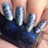 A manicured hand with Crystal Galaxy (m219) designs holding a polish by Maniology.