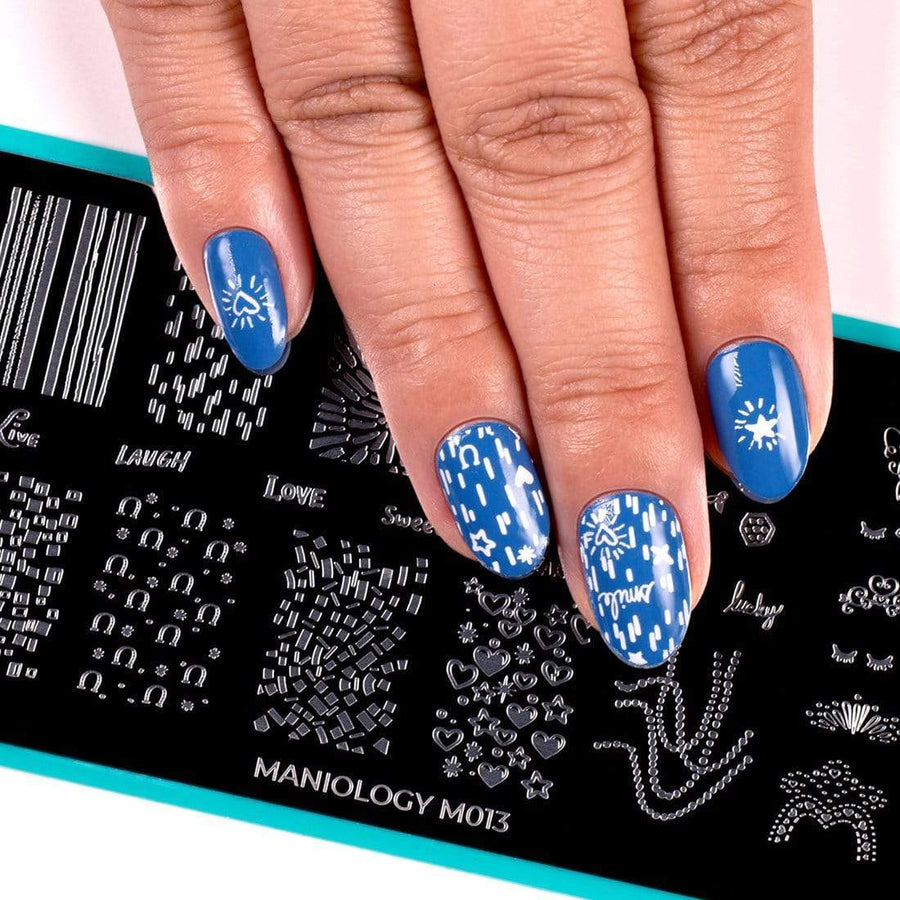 A manicured hand in blue with hearts, stars and horseshoe designs over a nail stamping plate by Maniology (m013).