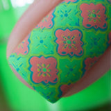 A manicured hand in green and pink with layered tile designs by Maniology (m029).