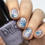 A manicured hand with snowflakes design holding a Mauve Cream Stamping Polish.