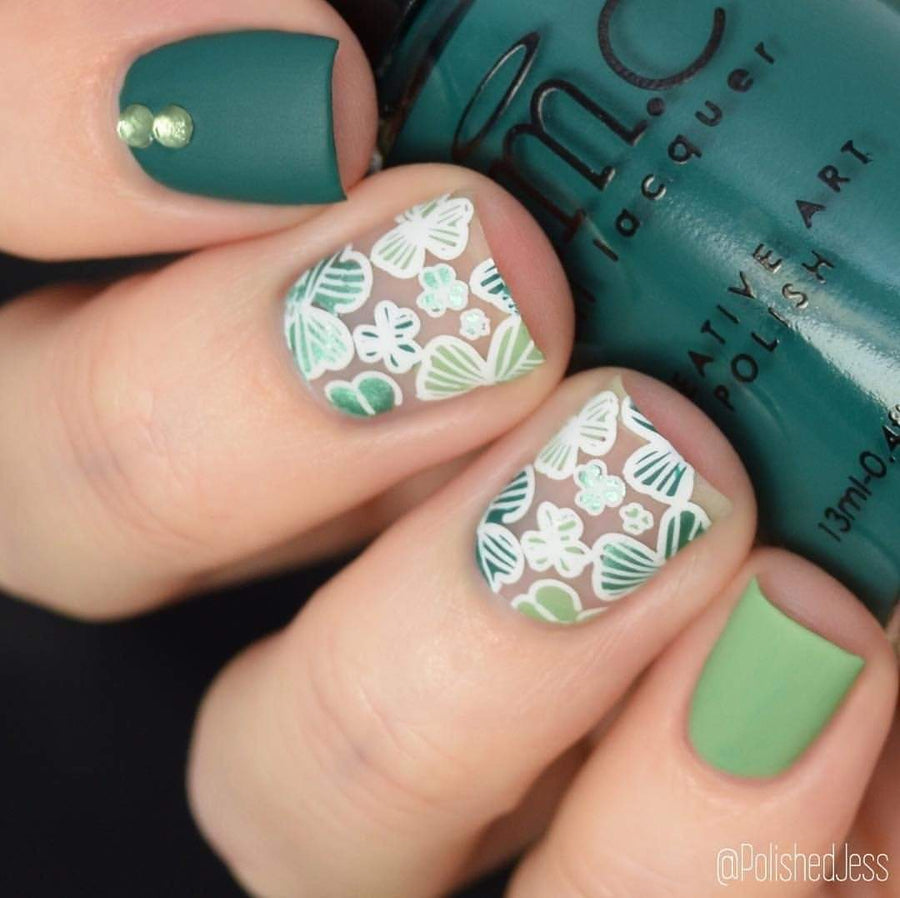 A manicured hand with clovers design by Maniology (m048) holding a polish.