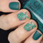 A manicured hand with snakes design holding a Deep Emerald Green Cream Stamping Polish.