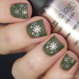 A manicured hand in green with snowflakes designs holding a polish by Maniology (m041).